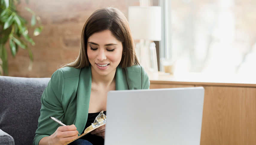 woman taken notes next to laptop